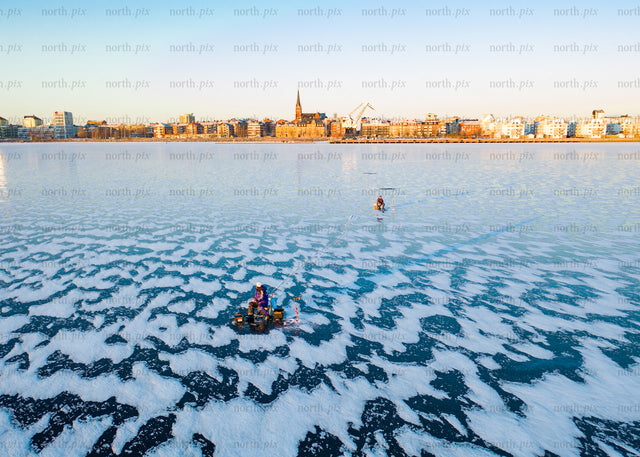 Winter cityscape view of frozen lake with people in morning light