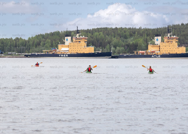 Kayakers paddling near docked icebreakers on overcast day