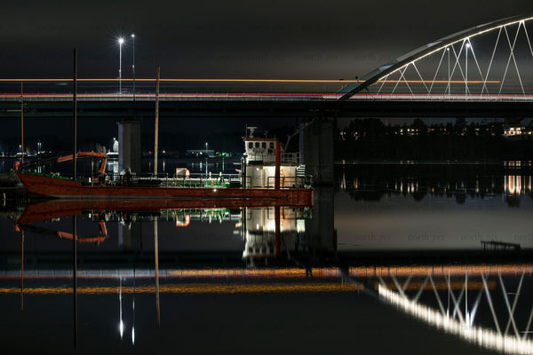 Cargo boat moored under illuminated bridge at night