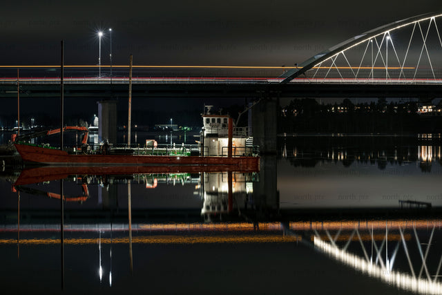 Cargo boat moored under illuminated bridge at night
