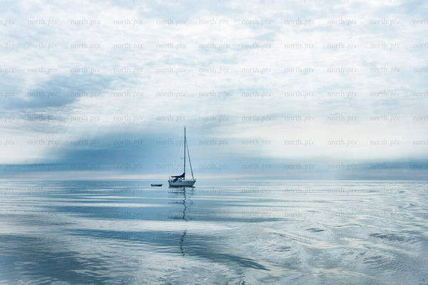 Sailboat anchored on calm sea under cloudy sky