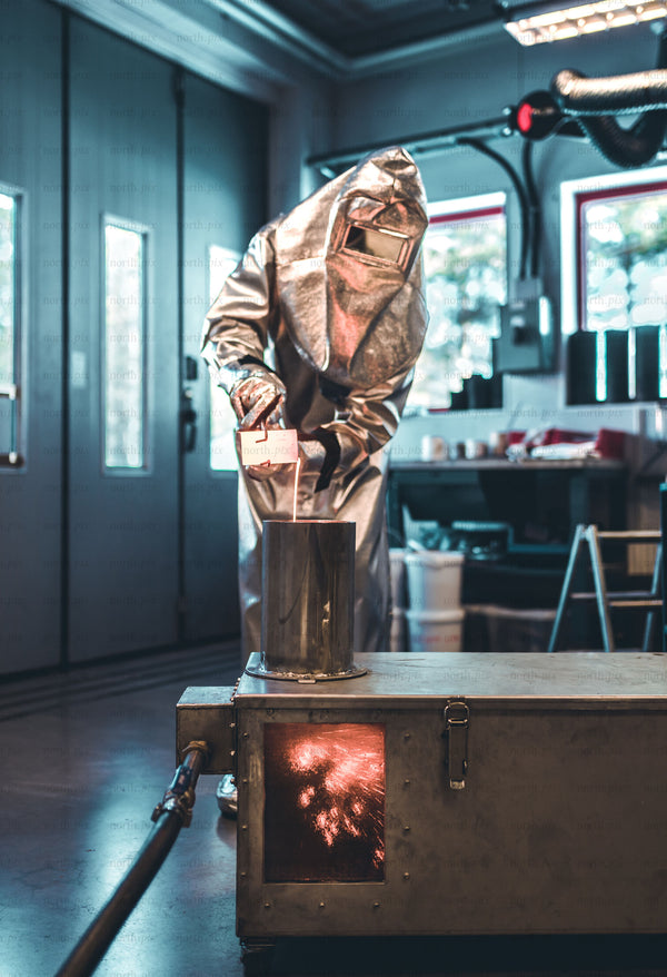 Worker in heat-resistant suit pouring molten metal in workshop