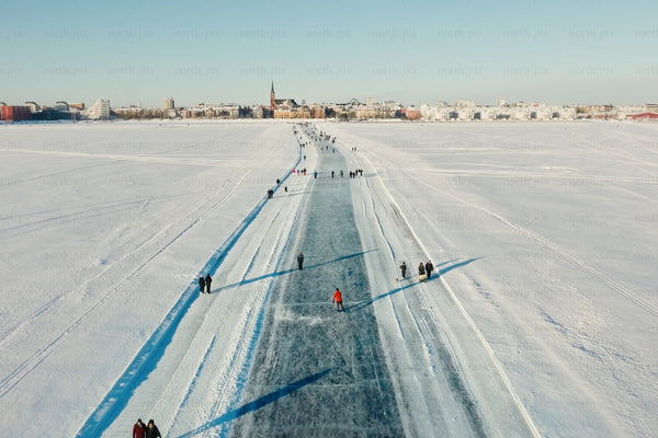 Ice path across snowy lake toward Luleå city center with skaters and snowy skyline