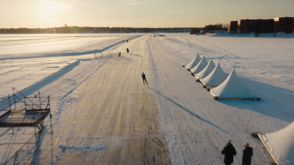 Man speed skating on frozen lake, Luleå - winter sunset aerial drone footage