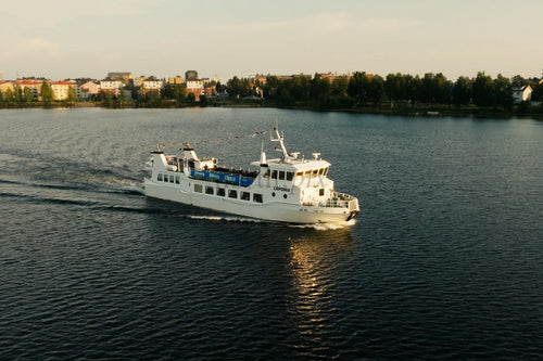 Vit passagerarfärja glider över lugn sjö nära Luleå centrum med träd och byggnader