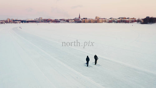 Längdskidåkning i vintersolnedgång på frusen sjö i Luleå, Sverige med stad i bakgrunden