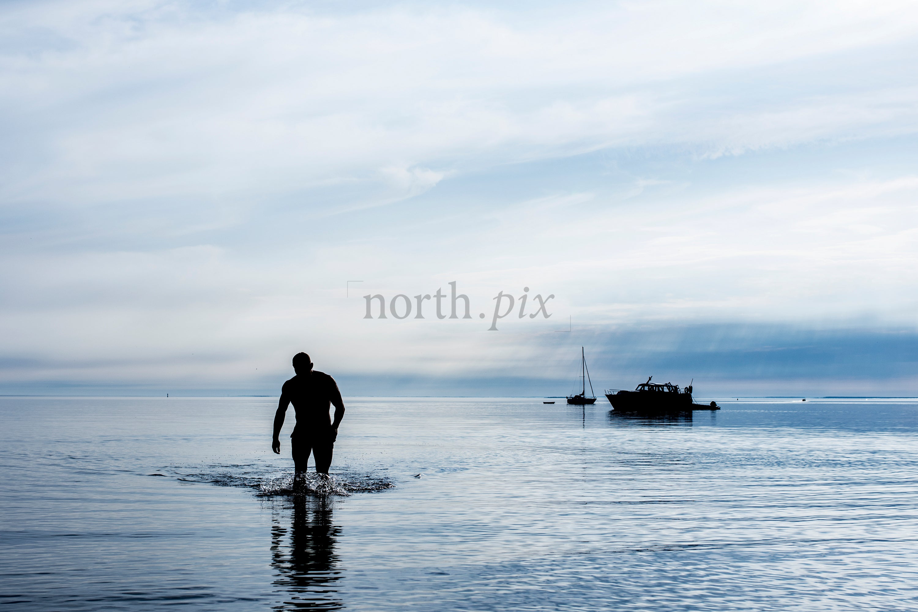 Silhouette of man walking in shallow sea at dawn