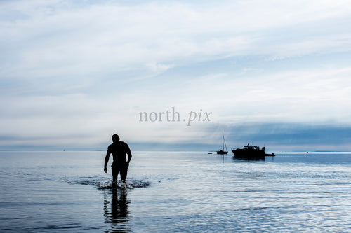 Silhouette of man walking in shallow sea at dawn