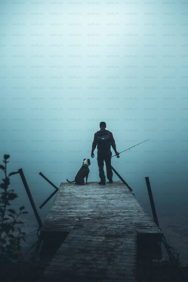Man fishing from dock with dog in fog