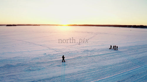 Vänner njuter av en vinterpromenad i solnedgången på en frusen sjö i Luleå, Sverige
