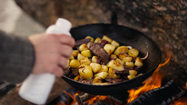 Cooking meat and potatoes in creamy sauce over open fire in winter, Luleå