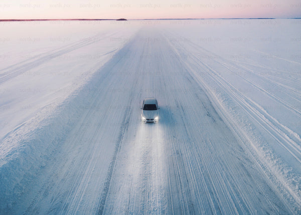 White car driving on a snowy ice road during sunset in winter