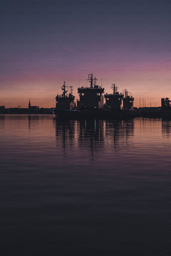 Silhouetted ships in harbor at dusk with reflections