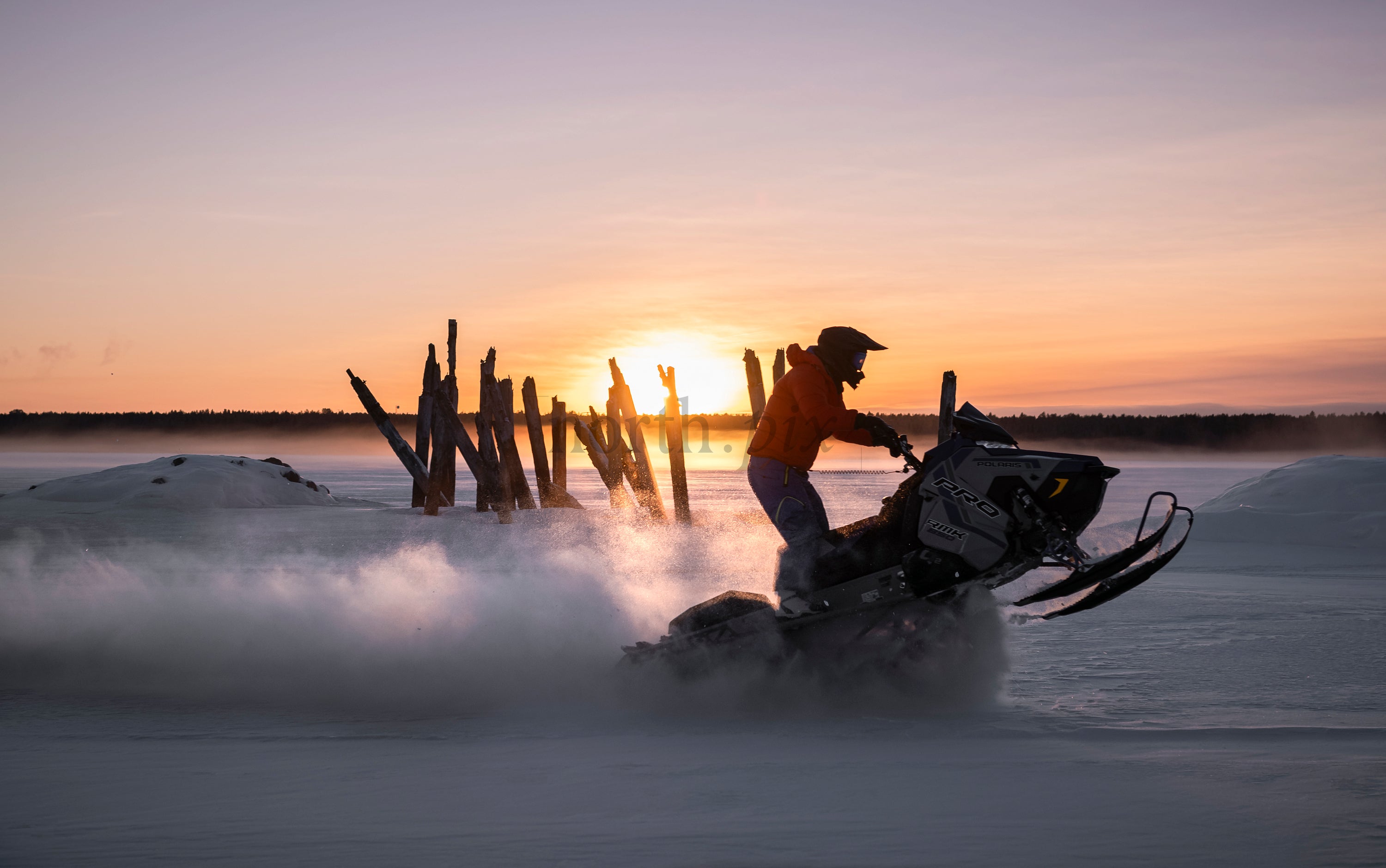 Snowmobile rider on a frozen lake at sunset