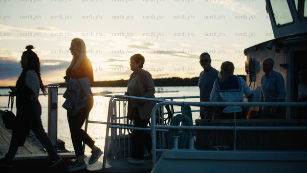 Friends and family disembark boat on pier in Luleå at sunset