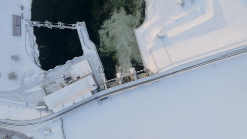 Flygfoto ovanifrån av en vattenkraftverksdamm som spiller vatten i snöig vinter