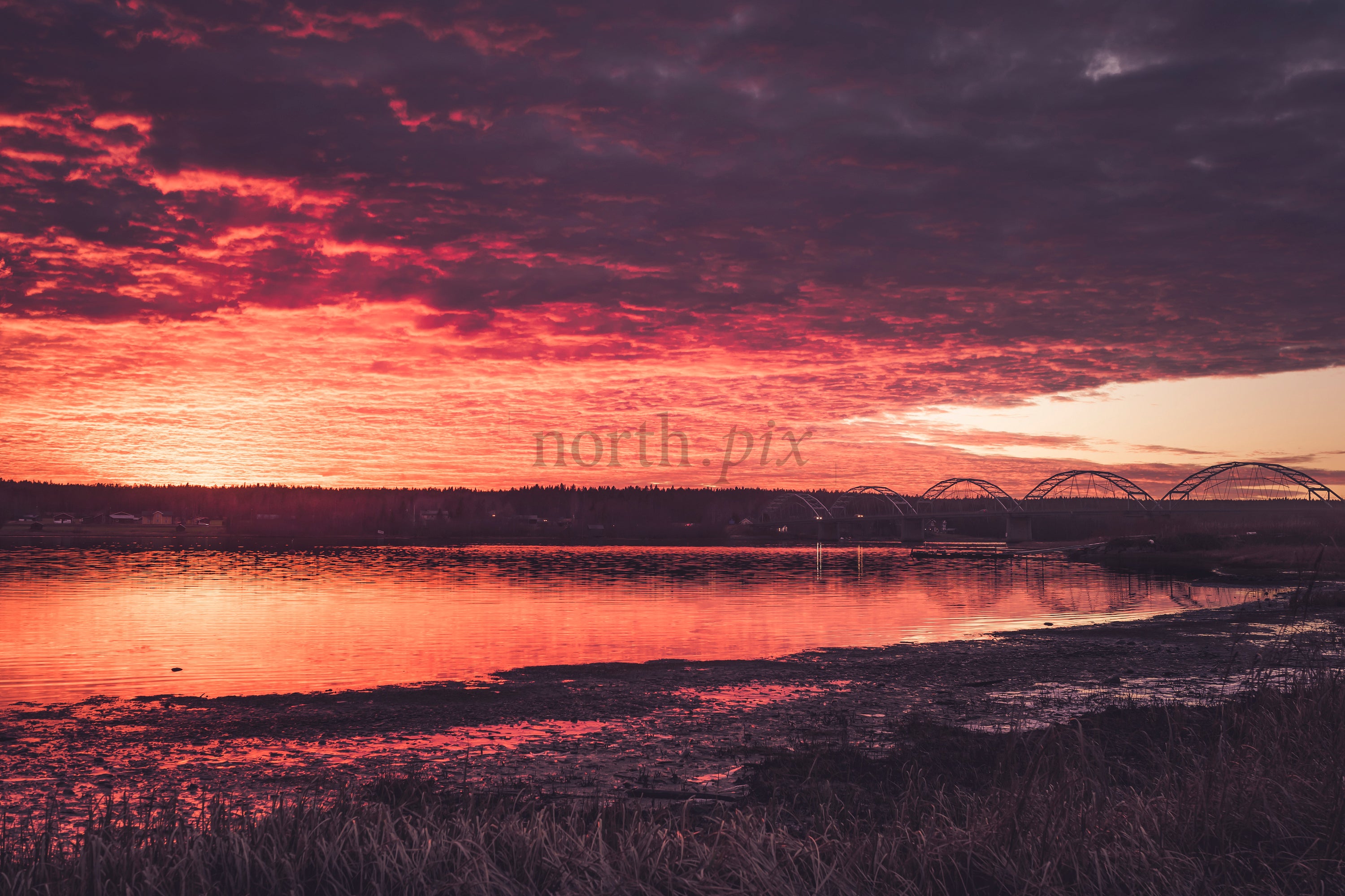 Arched bridge over river under red sunset sky