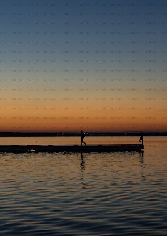Person walking on pier at sunset