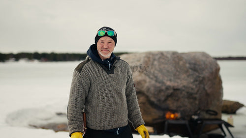 Man i vinterkläder vid eld i snöig, isig Luleå skärgård, Sverige