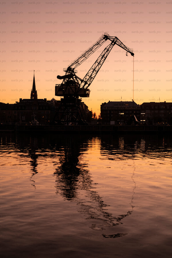 Silhouette of harbor crane and city at sunset