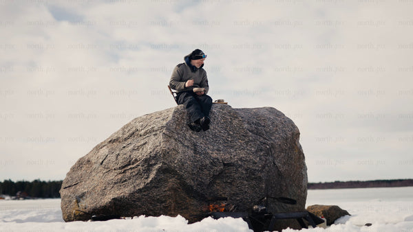 Man enjoys a warm drink by a fire on a frozen lake in the Luleå archipelago
