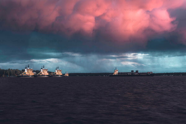 Cargo ship and tugboats under pink storm clouds