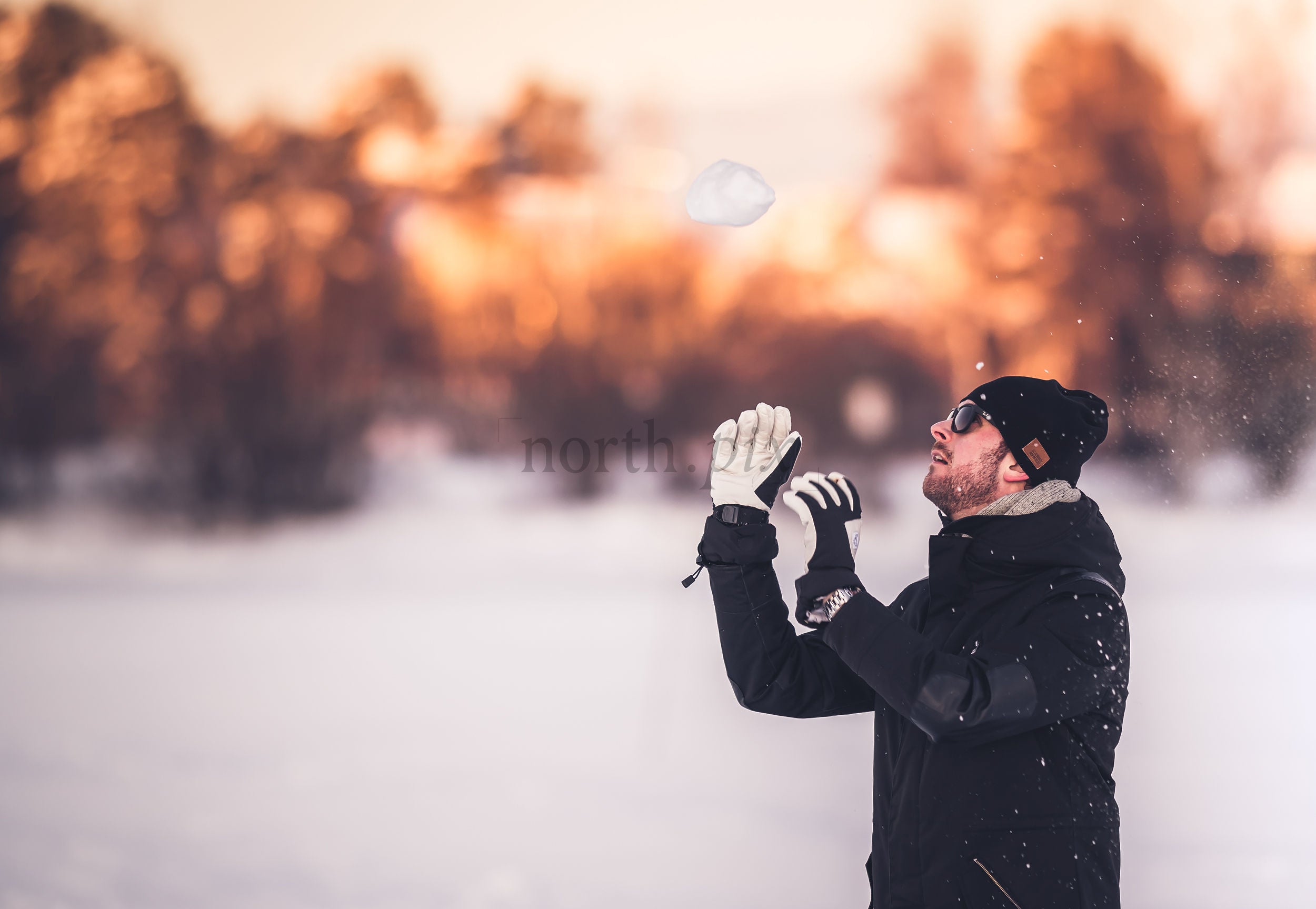 Man catching a snowball in a snowy field at sunset