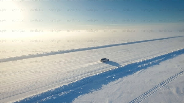 White car driving on a snowy ice road in Luleå, on a bright winter day