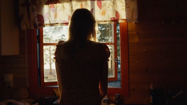 Woman opens window at golden hour in Swedish archipelago cabin