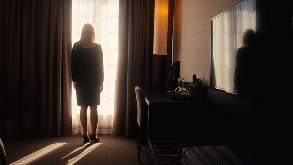 Businesswoman opens curtains to sunrise view in modern hotel room