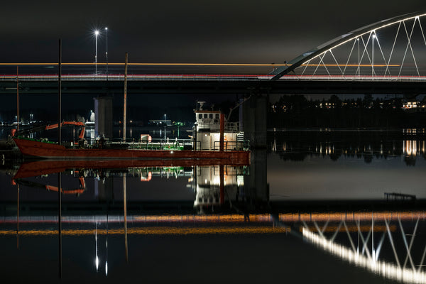 Red workboat moored under illuminated modern bridge at night