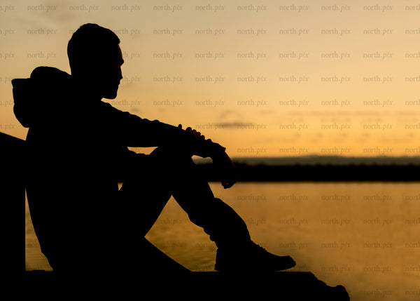 Silhouette of man sitting on dock at sunset