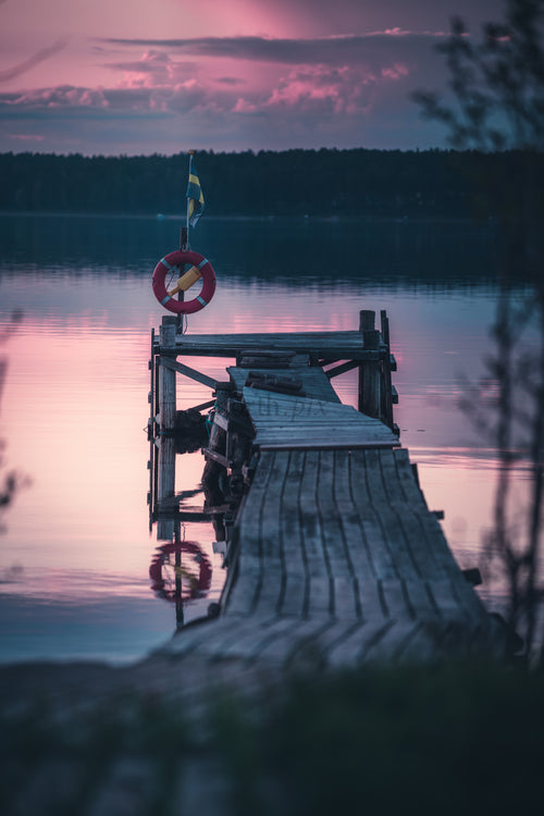 Träbrygga med livboj och svensk flagga i skymningen