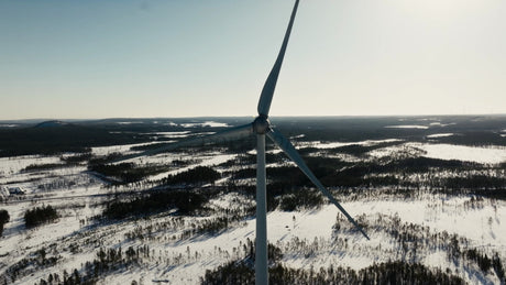 Wind Turbine Rotating in Snowy Winter Landscape: Aerial View of Renewable Energy