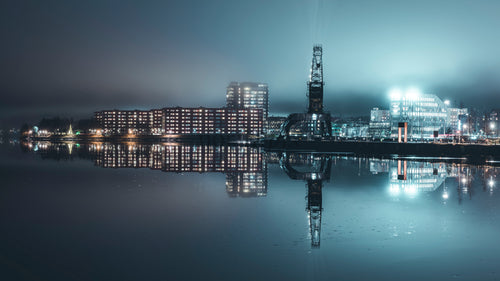 Industrikran och byggnader vid vattnet i nattpanorama