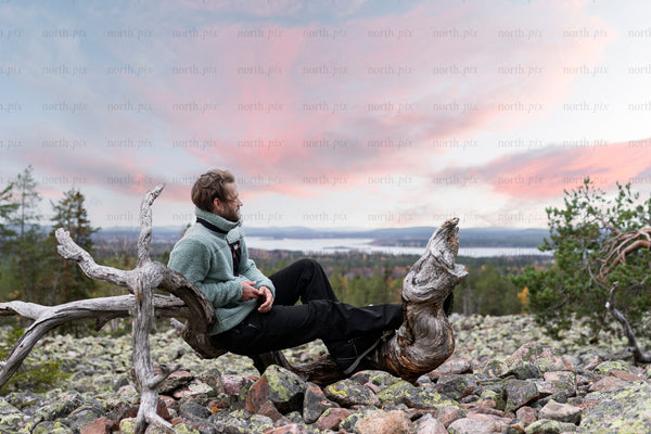 Man sitting on deadwood log on rocky hillside at sunset