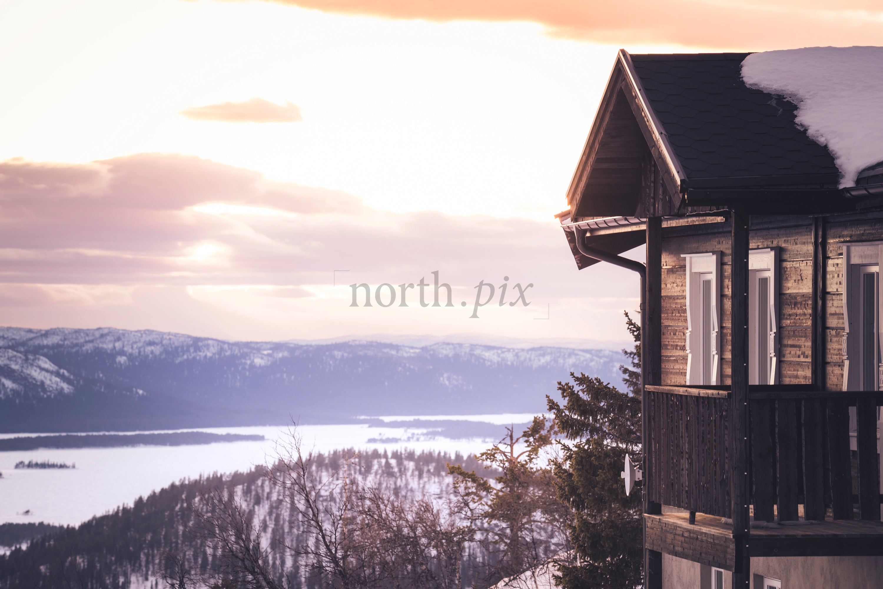 Wooden cabin balcony overlooking snowy lake at sunset