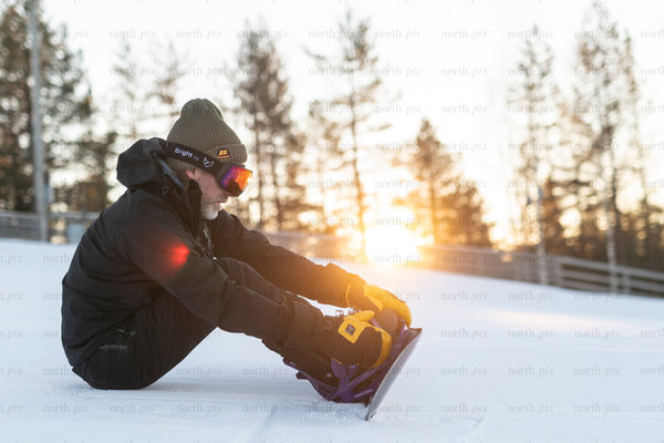 Man preparing snowboard at sunset, winter