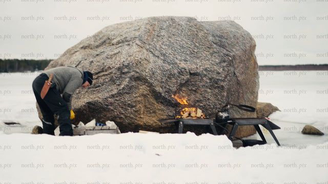 Winter cooking in the Luleå archipelago: Man prepares a meal by a campfire on a frozen lake