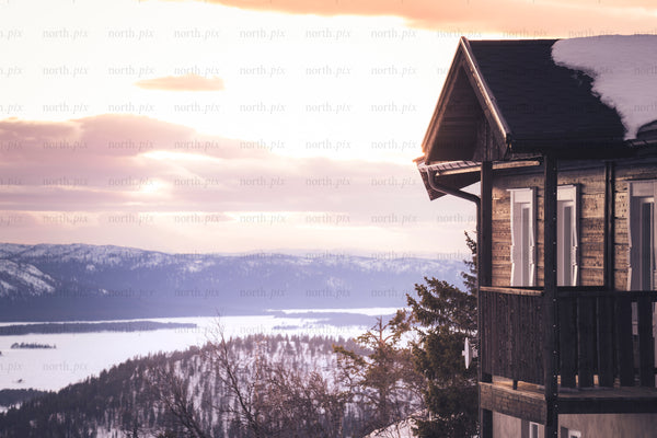 Wooden cabin balcony overlooking snowy lake at sunset