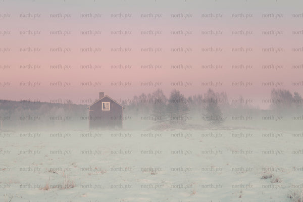 Small red house in snowy field at sunrise