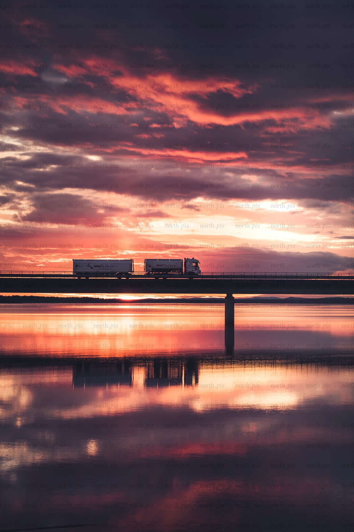 Truck crossing bridge at sunset with water reflection