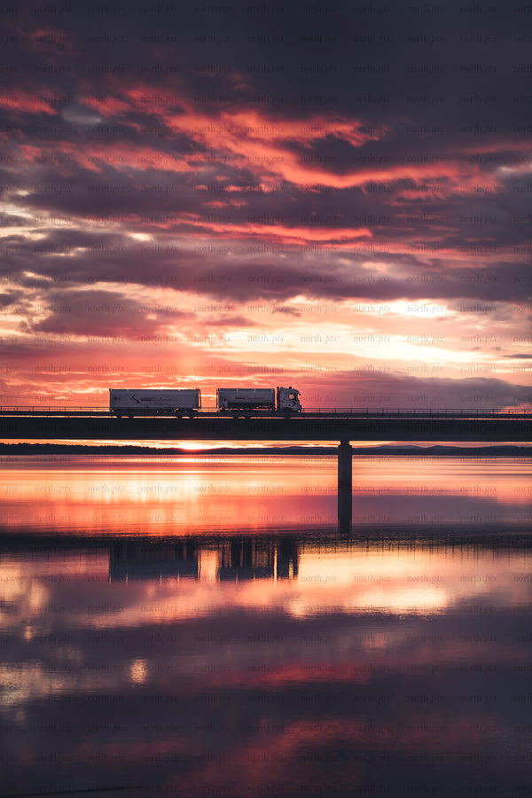 Truck crossing bridge at sunset with water reflection