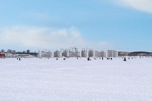 People ice fishing on frozen bay with waterfront apartments, winter