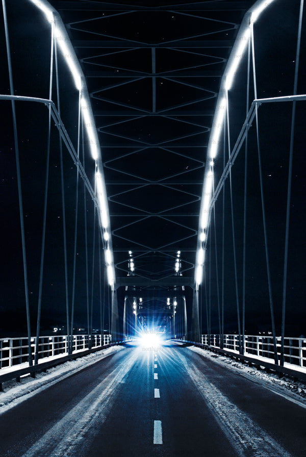 Car with bright headlights crossing a lit truss bridge at night