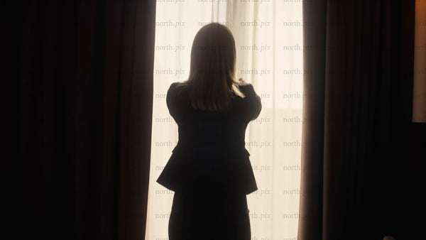 Businesswoman opens curtains in hotel room at sunrise in Luleå