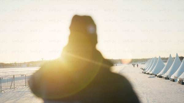 Winter sunset over frozen landscape with man and tents in Luleå