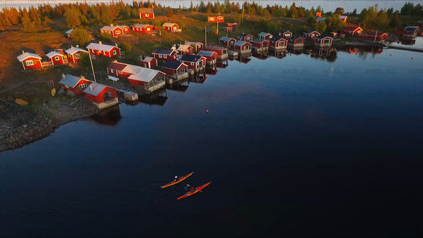 Kayakers paddle past red cabins in the Luleå archipelago at sunset