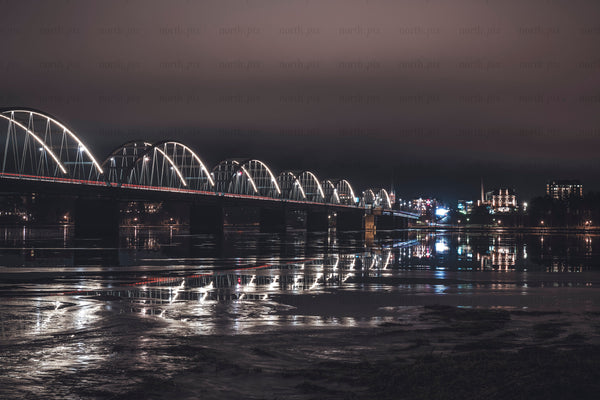 Illuminated arched bridge over partly frozen river at night