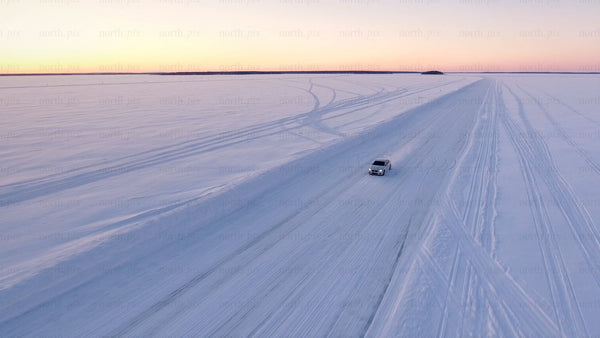 Driving on ice: Aerial view of car on snow-covered winter road in Luleå archipelago at sunset